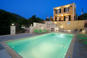 A swimming pool with lounge chairs, a stone wall, and a building with balconies.