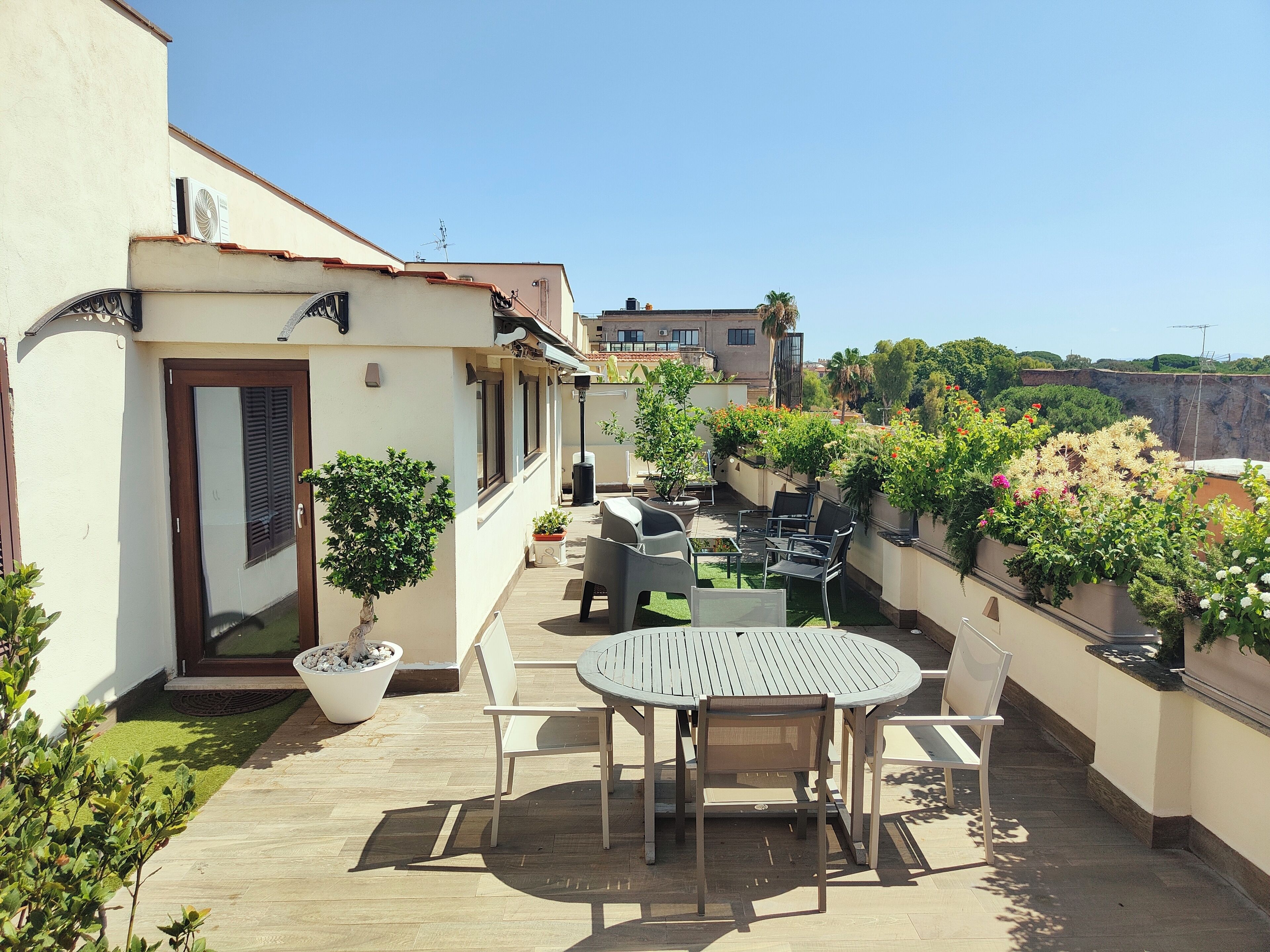 A rooftop patio with a round table and chairs, potted plants, and a view of the cityscape.