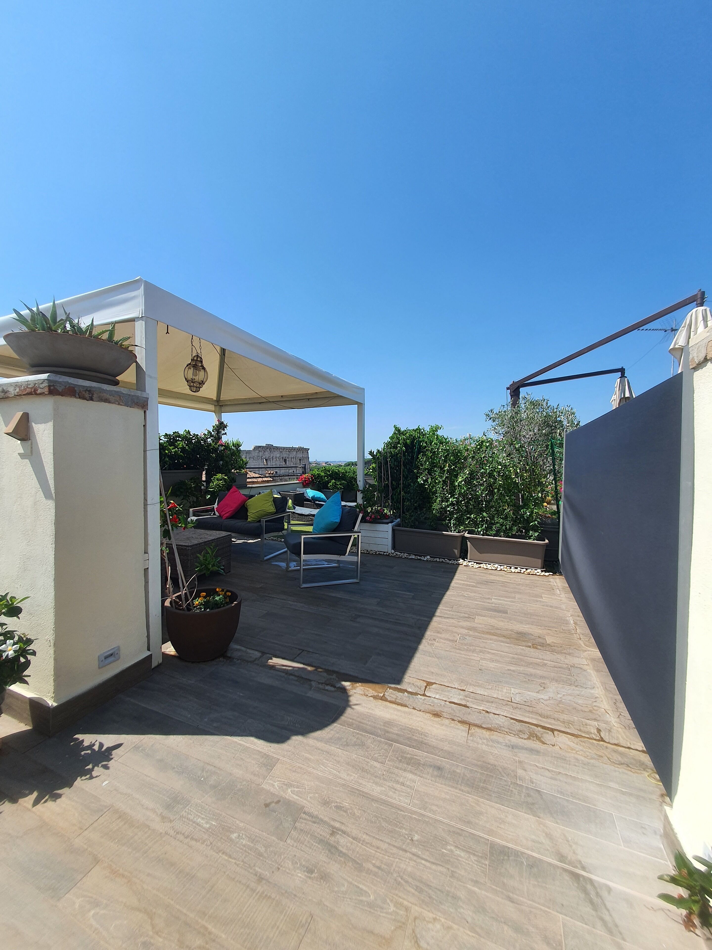 A covered patio area with outdoor furniture, a pergola, and potted plants.