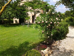 Ein Garten mit Rosenbusch, einem Steinhaus und einem Kiesweg.