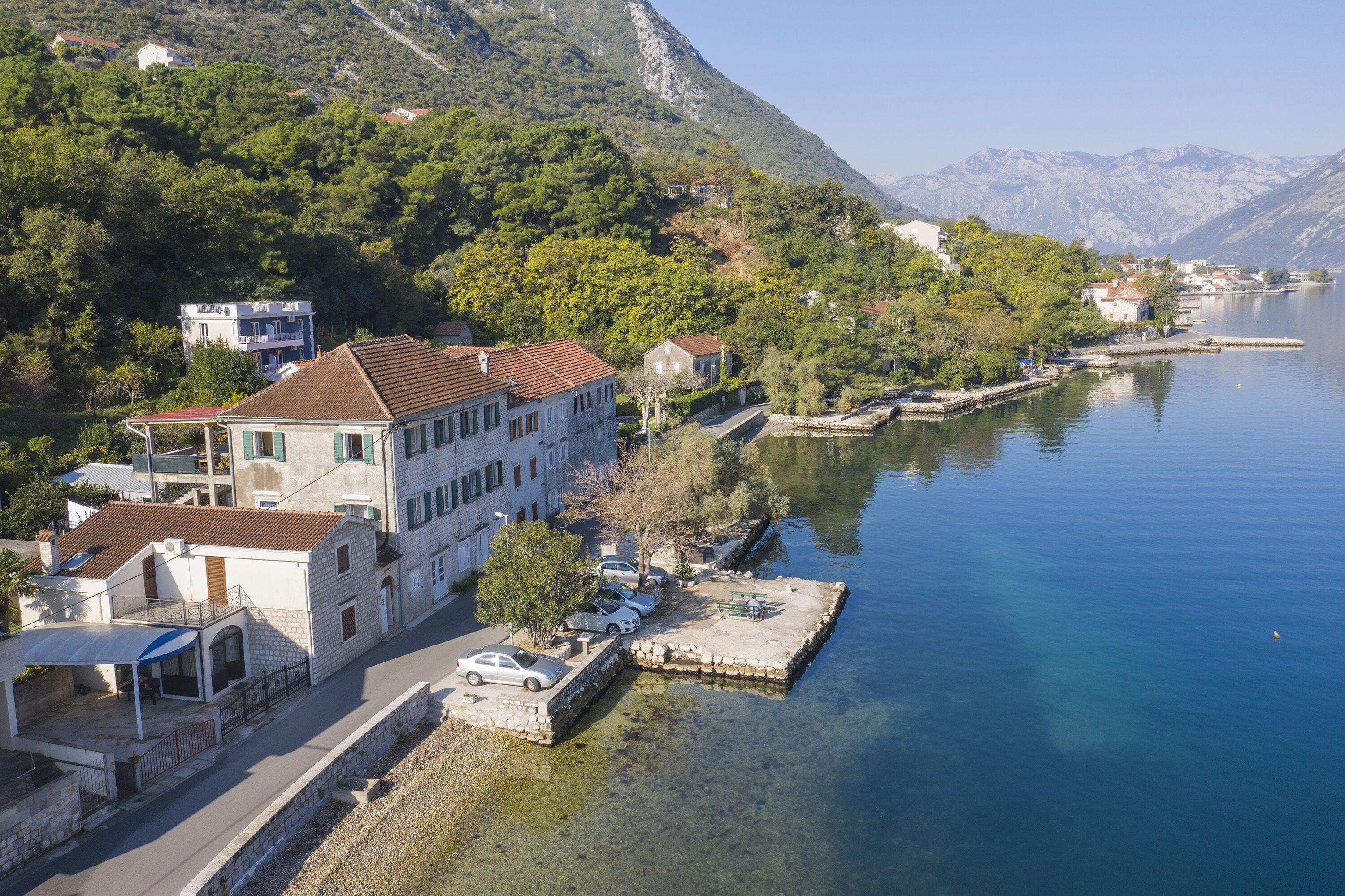 A lakeside property with a stone dock, a covered outdoor seating area, and a view of the lake and mountains.