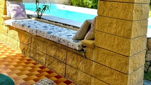 Un espace extérieur lumineux, aménagé avec des sièges, une piscine, des piliers en pierre et un sol carrelé.