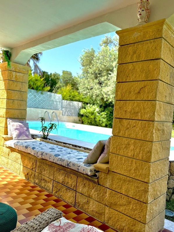 A sunlit outdoor seating area with a pool, stone pillars, and a tiled floor. - Villa AnnaStella a Corner of Paradise with Pool,AC, WiFi, SmartTV/Netflix/Disney (Sicilia)