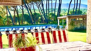 Un espace aménagé au bord de la piscine, avec des chaises à rayures et une table, entouré d’un mur en pierre et offrant une vue sur un paysage montagneux.
