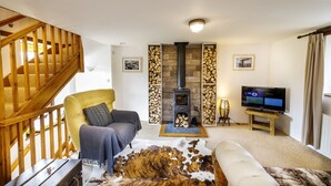 Una sala de estar acogedora con una escalera de madera, un sofá, un televisor y una chimenea.