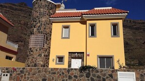 A two-story building with a yellow facade, a stone tower, and a red-tiled roof. - Modern Villa With Stunning Mountain Views (Mogan)