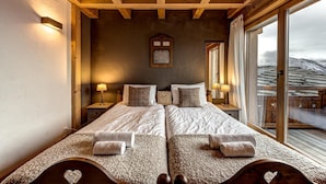 Un lit double avec deux oreillers et une table de chevet avec une lampe, un plafond en bois et une grande fenêtre donnant sur un paysage enneigé.