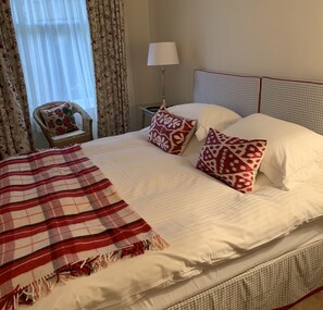 A neatly made bed with a checkered blanket, two patterned pillows, and a chair with a floral cushion.