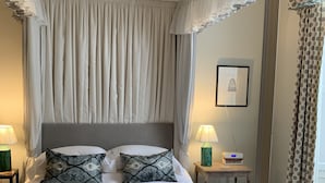 Un dormitorio ordenado con una cama con dosel, lámparas de noche, una mesita con un radio y un cuadro en la pared.