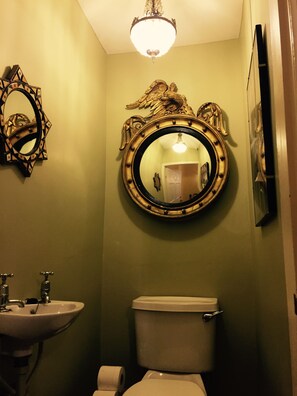 A bathroom with a round mirror, sink, toilet, and a chandelier.