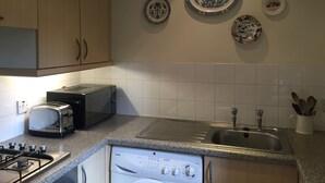 Una cocina con estufa a gas, tostadora, microondas, pileta y lavavajillas.