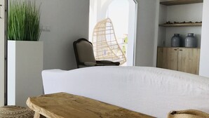 Ein Schlafzimmer mit einem Bett, einer Holzbank, einem Korbstuhl, einer Topfpflanze und einem Regal mit Gläsern.