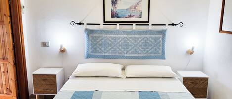 A neatly arranged hotel room with a bed, two bedside tables, a wall-mounted picture, and a patterned headboard.