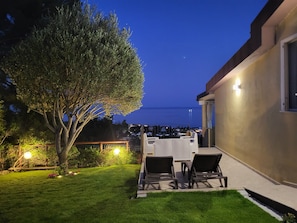A patio with outdoor furniture, a tree, and a view of the sea at dusk.