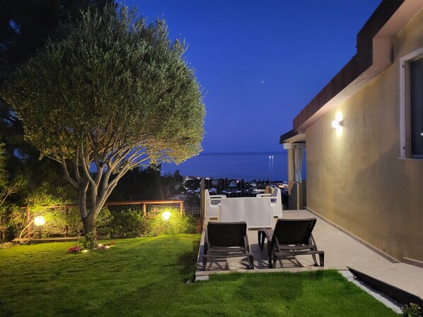 A patio with outdoor furniture, a tree, and a view of the sea at dusk.
