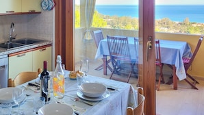 A dining area with a table set for two, a kitchen with a sink, and a view of the ocean. - Splendid Sea View Villa with Privacy and Garden, Just 700m from the Beach! (Costa Rei)