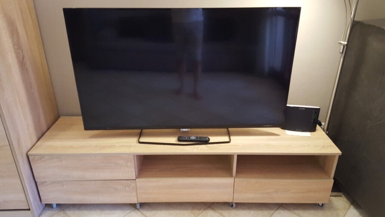 En tv-apparat med platt skärm står på ett TV-bord i trä, och en fjärrkontroll ligger bredvid.