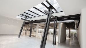 Un intérieur spacieux et moderne, doté d’un plafond haut et de puits de lumière, avec des poutres apparentes et un aménagement épuré et minimaliste.