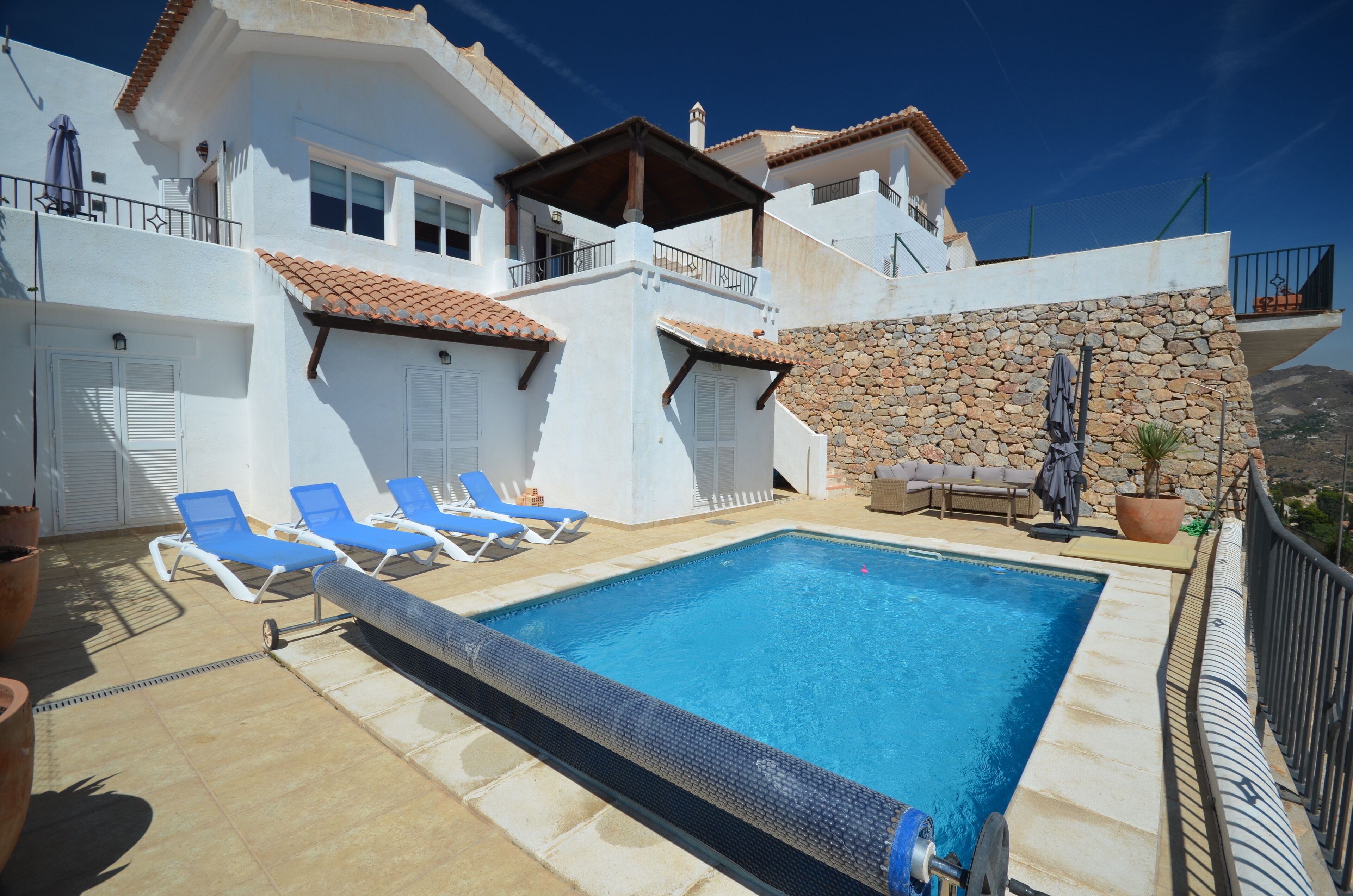A poolside area with a swimming pool, blue lounge chairs, and a stone wall.
