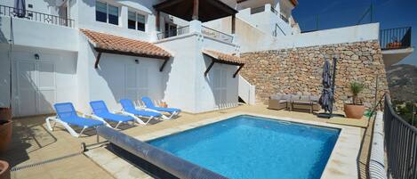 A poolside area with a swimming pool, blue lounge chairs, and a stone wall.