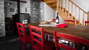 Een eetgedeelte met een houten tafel, rode stoelen, een stenen muur, een houten trap en een zwarte kookplaat.