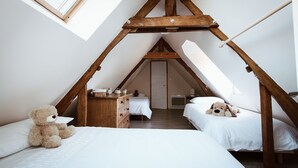 Een gezellig slaapkamer onder de dakpannen, met twee bedden, houten balken, een dakraam en een teddybeer op een van de bedden.