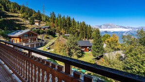 Un albergue de montaña con varias cabañas, una terraza de madera y vistas al bosque y las montañas circundantes.