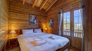 Un dormitorio de cabaña de madera con una cama grande, dos cuadros en la pared y una ventana con cortinas.