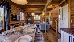 Interior de una cabaña de madera con una mesa de comedor para cuatro personas, un sofá y una zona de cocina.