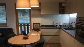 Une cuisine moderne avec une table en bois, des chaises noires, une grande fenêtre et un four encastré.