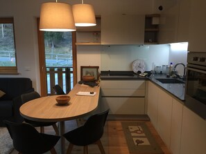 A modern kitchen with a wooden table, black chairs, a large window, and a built-in oven.