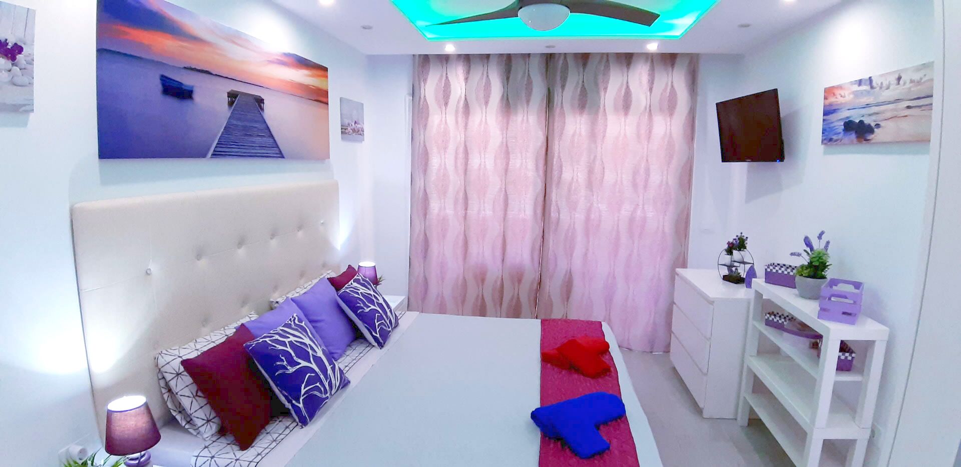 A modern bedroom with a large bed, a headboard, a bedside table, a TV, and a window with curtains.