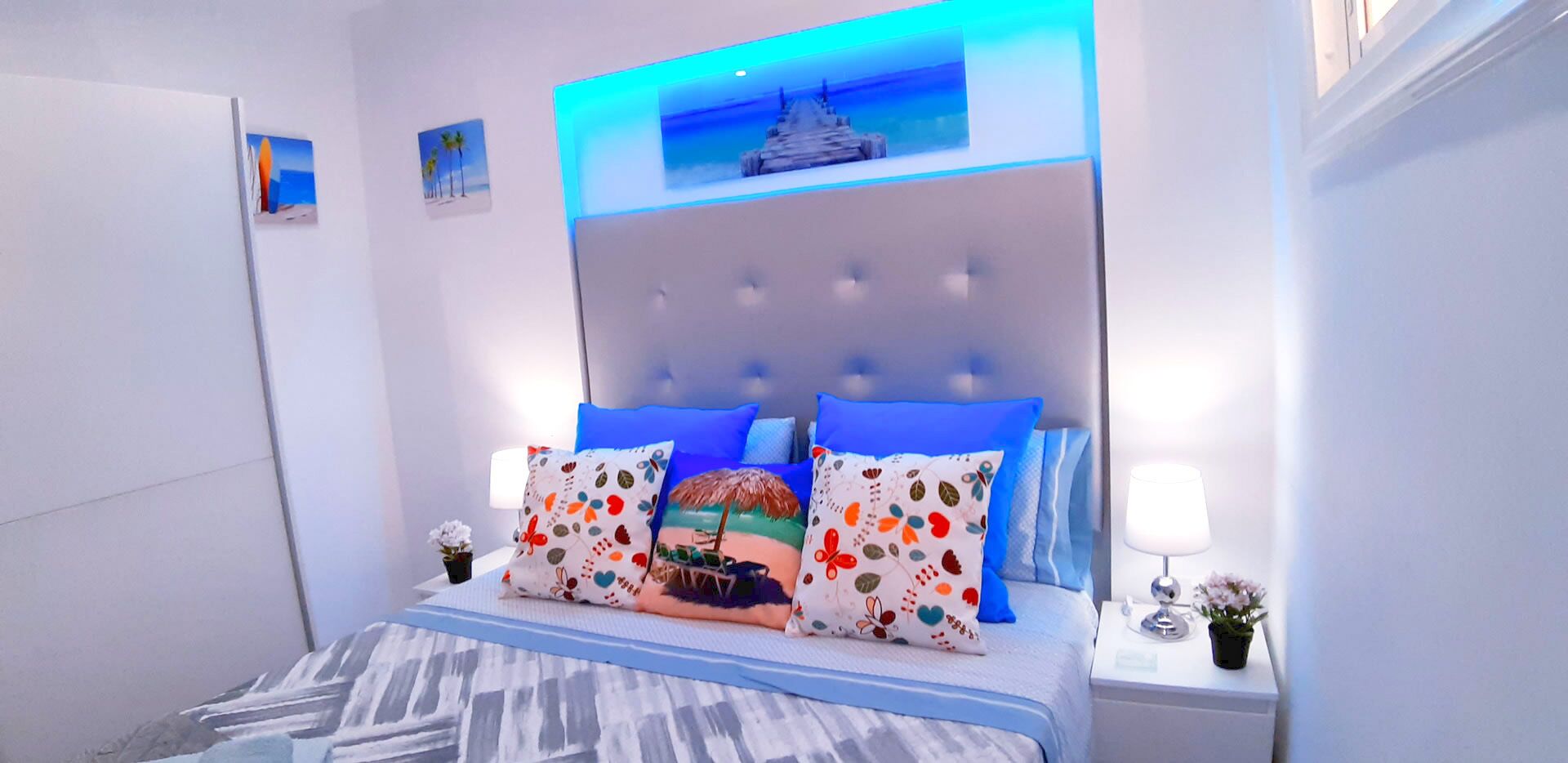 A modern bedroom with a tufted headboard, a bed with blue bedding, and decorative pillows.