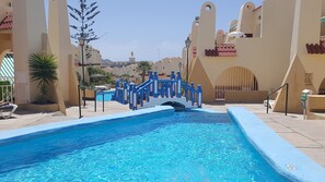 A swimming pool with a blue border, surrounded by beige walls with arched doorways and a decorative blue staircase.