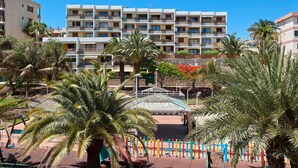 A multi-story hotel with balconies, palm trees, and a clear blue sky.