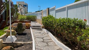 A stone pathway leading to a building with a white fence and greenery.