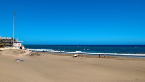 A beach with a lifeguard tower, a lifeguard chair, and a boat on the sand.