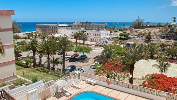 A pool area with lounge chairs and a view of the beach and ocean.
