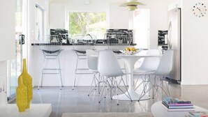 Una cocina moderna con armarios blancos, un comedor con sillas blancas y una botella decorativa amarilla.