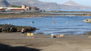 A beach with rocky shores, a few people, and a distant mountain range.