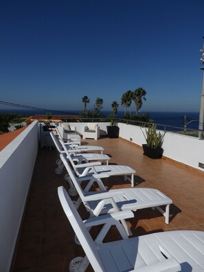 Une terrasse sur le toit, dotée de chaises longues blanches et de plantes en pot, offrant une vue imprenable sur la côte.