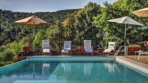 A swimming pool with clear water, surrounded by lounge chairs and umbrellas, set against a backdrop of lush greenery and hills. - Chiusarella Arceno Rentals Club Chianti Villa exclusive Pool Concierge freeWiFi (CASTELNUOVO BERARDENGA)