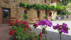 A stone building with a rustic exterior, a gravel courtyard, and various potted plants and flowers. - Chiusarella Arceno Rentals Club Chianti Villa exclusive Pool Concierge freeWiFi (CASTELNUOVO BERARDENGA)