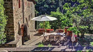 A stone building with a patio area featuring a table and chairs, surrounded by potted plants and a view of a vineyard. - Chiusarella Arceno Rentals Club Chianti Villa exclusive Pool Concierge freeWiFi (CASTELNUOVO BERARDENGA)