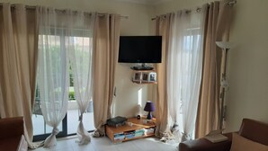 Ett vardagsrum med en platt-TV som är monterad på väggen, en bokhylla med böcker och dekorativa föremål, ett soffbord och en soffa.