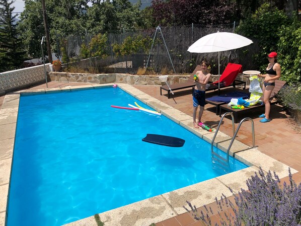 Une piscine bordée de pierres, un fauteuil de relaxation et une table sur laquelle sont posés divers objets.