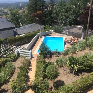 Ein rechteckiger Swimmingpool, umgeben von einem weißen Zaun, mit einer gepflasterten Liegefläche und einigen entspannten Personen in der Nähe.
