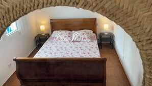 A cozy bedroom with a wooden bed, floral bedding, two bedside lamps, and a unique curved ceiling.