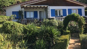 A two-story house with a wooden roof, blue shutters, and a small porch with a railing.
