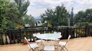 A patio with a round table and white chairs, surrounded by a black metal railing.